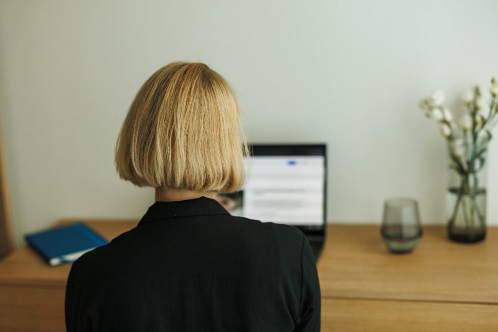 Kerstin Stock, eine blonde und dunkel gekleidete Frau, ist von hinten zu sehen und sieht auf einen eingeschalteten Laptopbildschirm während eines Coachings.