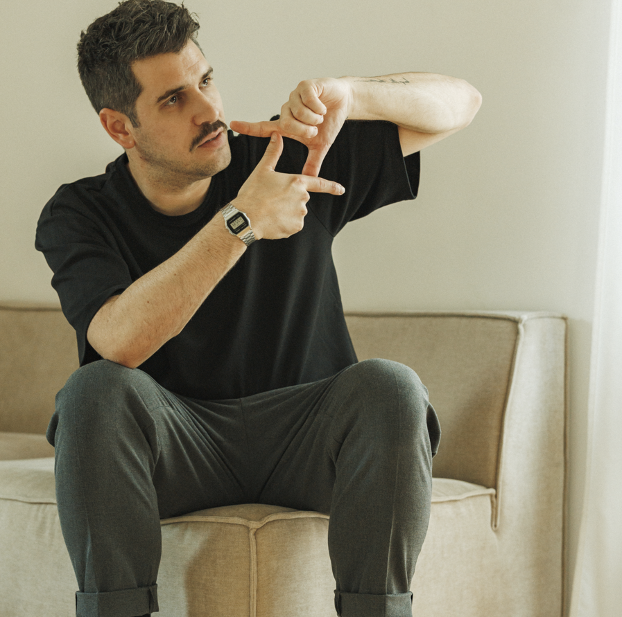 Ein Mann namens Tobias Schneider sitzt auf einer Couch und zeigt mit seinen Fingern ein Quadrat.