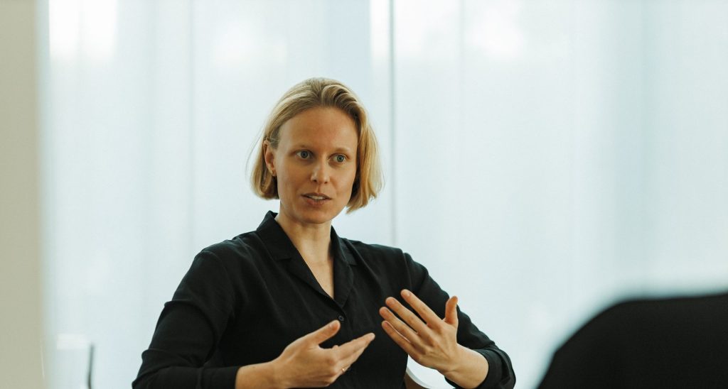 Eine blonde und schwarz gekleidete Frau gestikuliert erklärend mit ihren Händen.