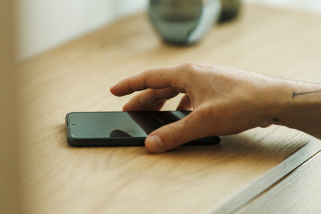 Eine Hand greift nach einem schwarzen Smartphone, das auf einer Holzunterlage liegt.