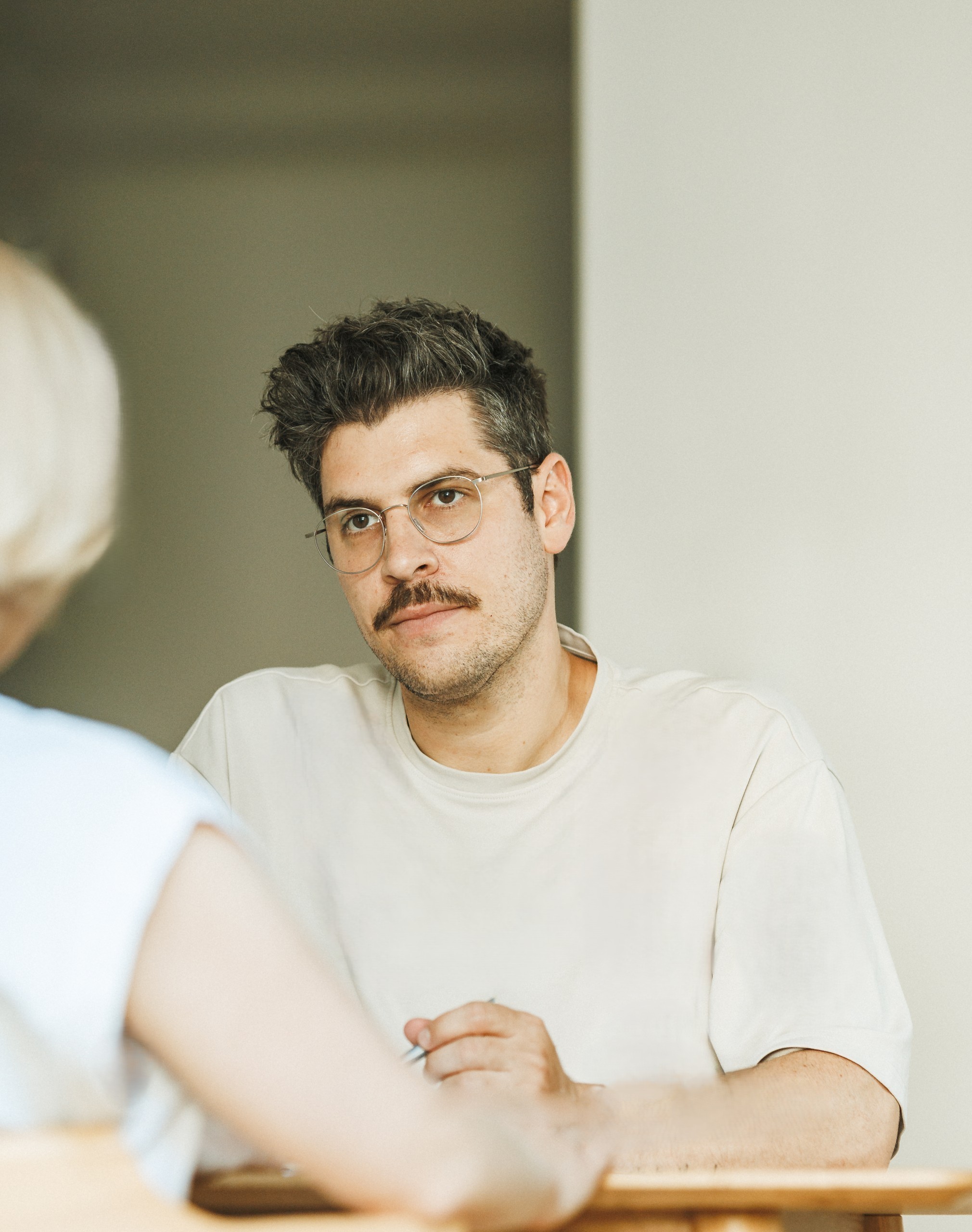 Ein Mann namens Tobias Schneider schaut eine gegenübersitzende Frau konzentriert während einer Mediation an.